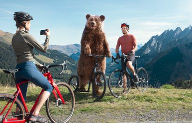 Ein Bär posiert für ein Foto mit zwei Radfahrer:innen